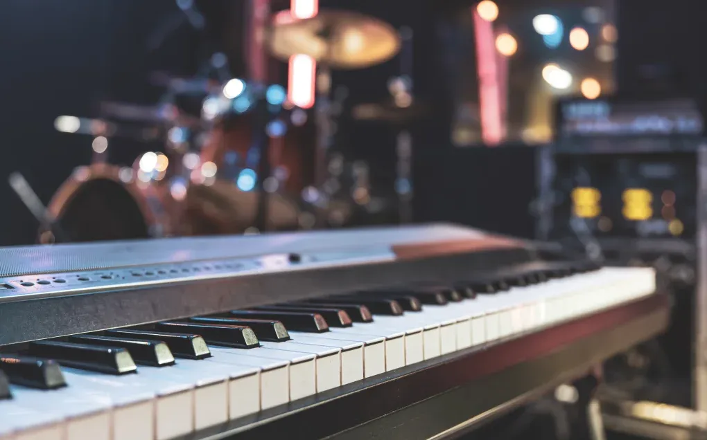 An electronic keyboard set up on stage in front of a drum kit and stage lights